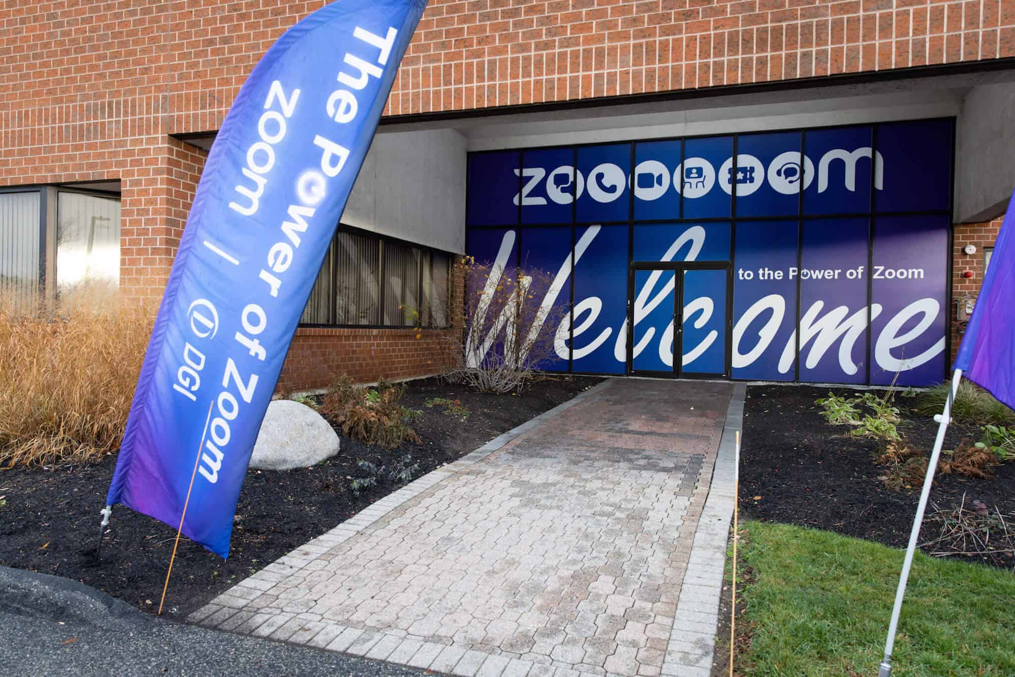 Trade show signage covering the glass entrance to a brick building. Two additional banners are set up beside a stone walkway that leads up to the building's front door.