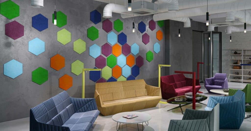 Office common space with multicolor couches and arm chairs arranged in a circle. Behind the seating area is a grey wall decorated with colorful hexagon decals.