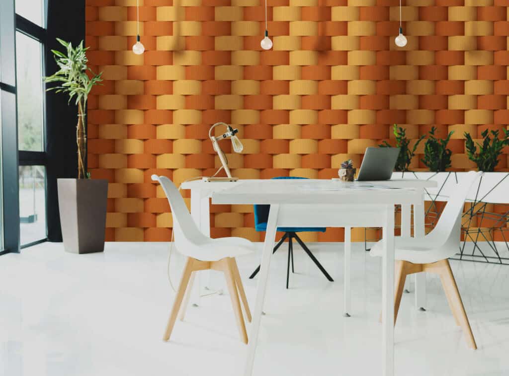 A communal work area in an office featuring a white table and three chairs. A plant is placed in the room's left corner, where floor-to-ceiling windows meet a textured wall.